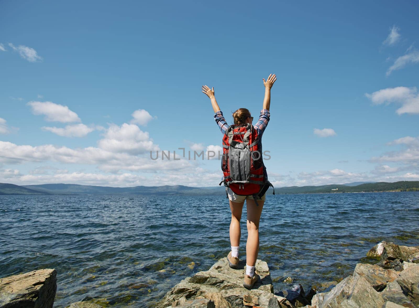 Female hiker with raised arms standing on rock by the sea