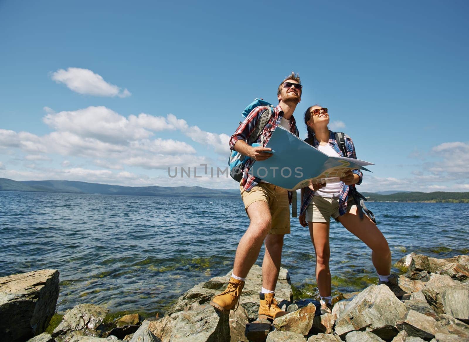 Amorous hikers with map looking upwards by the seaside