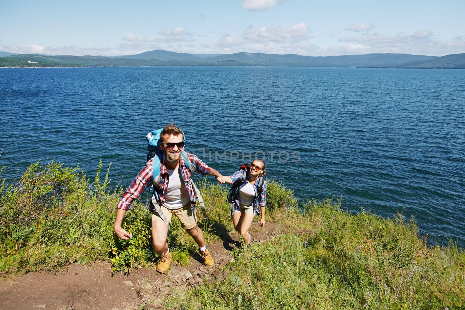 Happy young traveler helping his girlfriend to climb on mount