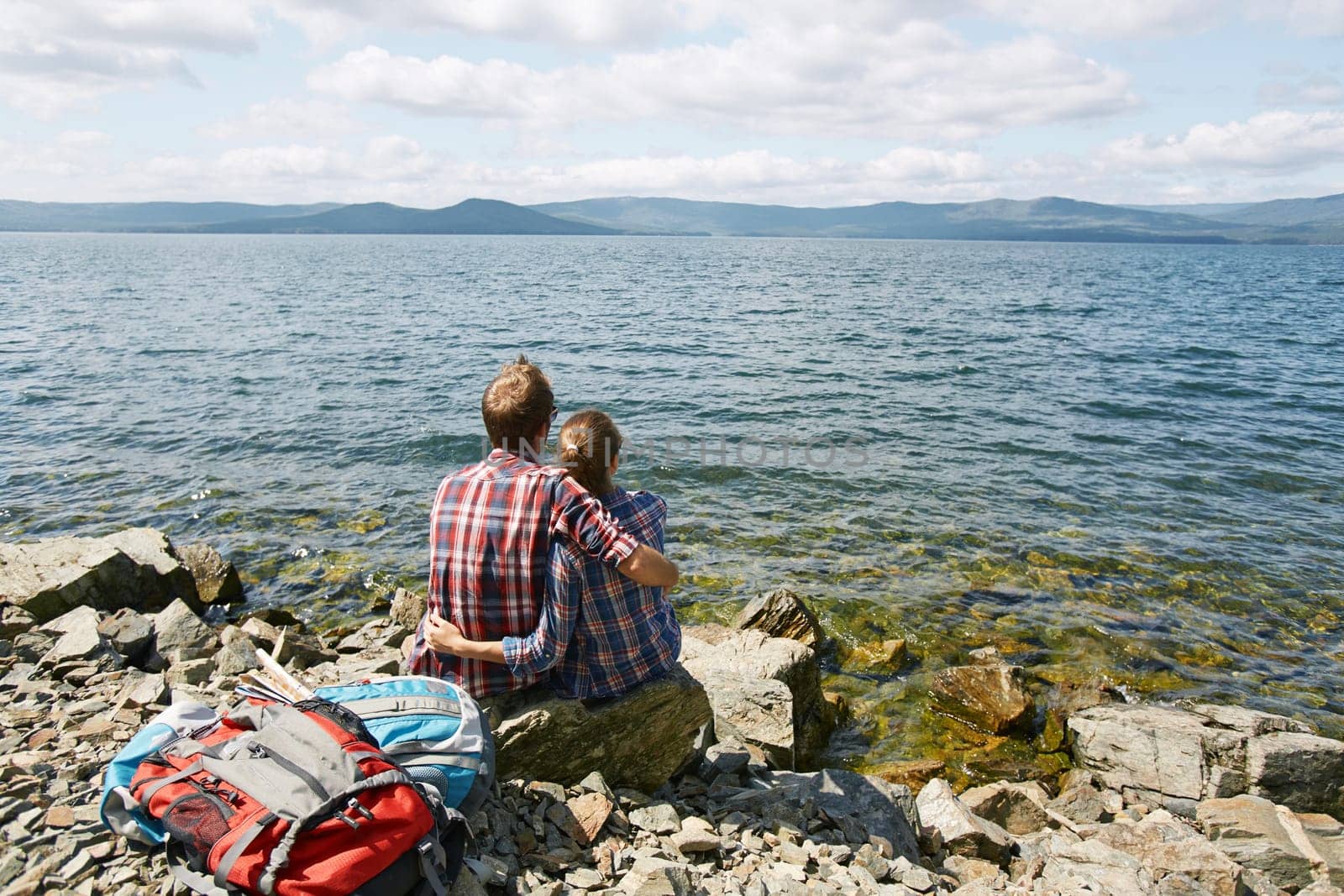 Rear view of amorous romantic couple in embrace sitting by the sea