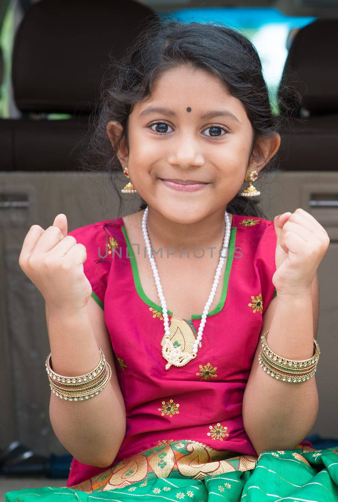 Excited Indian girl sitting in car smiling, ready to vacation. Asian child in traditional dress.