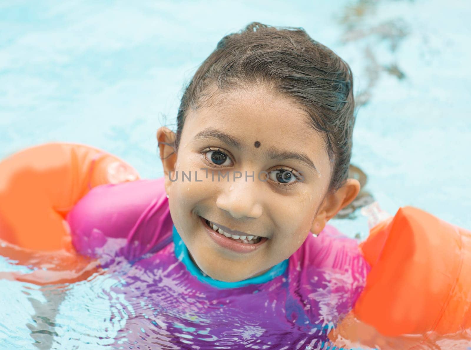 Indian child learning swimming in pool. Asian kid in swimmer class with float bands.