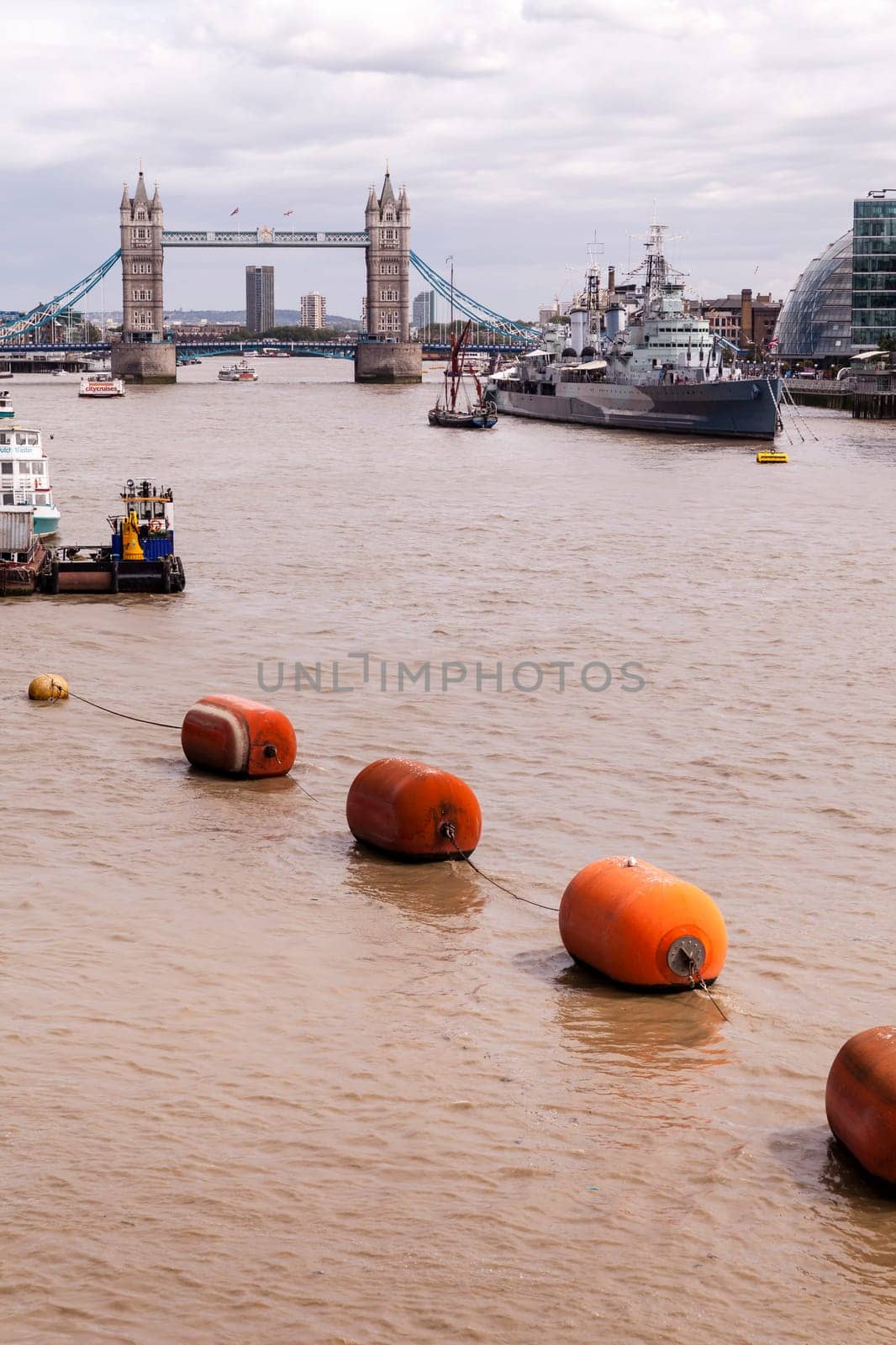 Editorial: London, United Kingdom - August 04, 2015: Thames River flowing towards the Tower Bridge, while passing the moored battleship HMS Belfast. Shot taken on London Bridge looking eastwards.