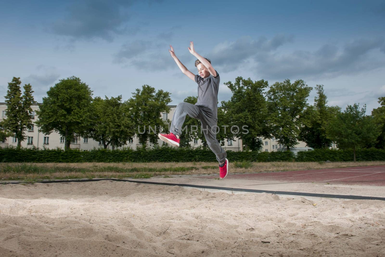 Side frontal full body view of a male young teenager frozen while jumping into a long jump pit