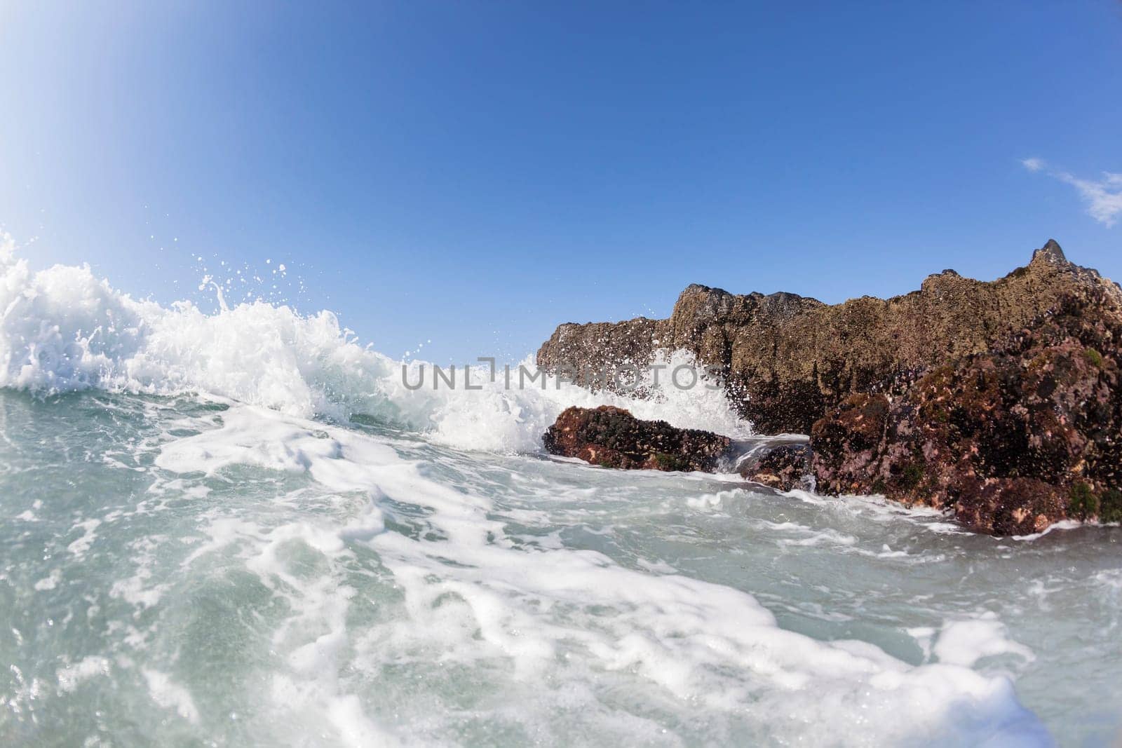 Ocean waves shore break crashing into rocks along beach coastline swimming closeup detail.