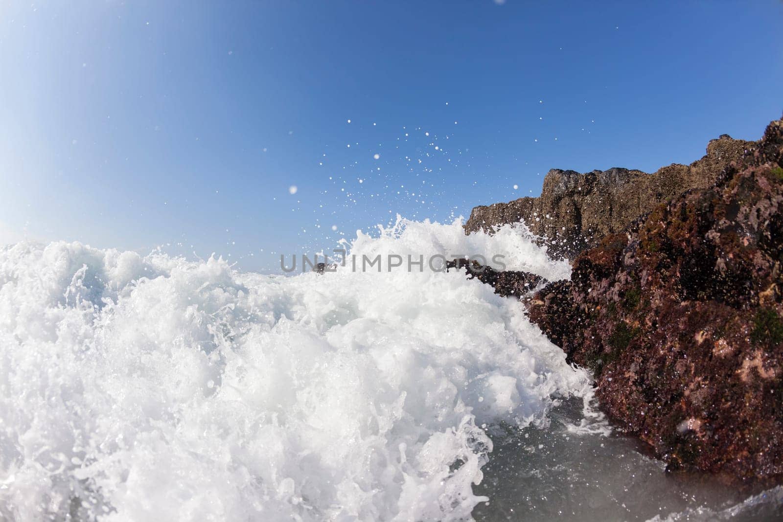 Ocean waves shore break crashing into rocks along beach coastline swimming closeup detail.