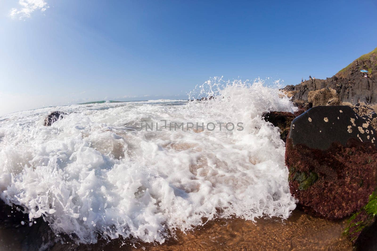 Ocean waves shore break crashing into rocks along beach coastline swimming closeup detail.