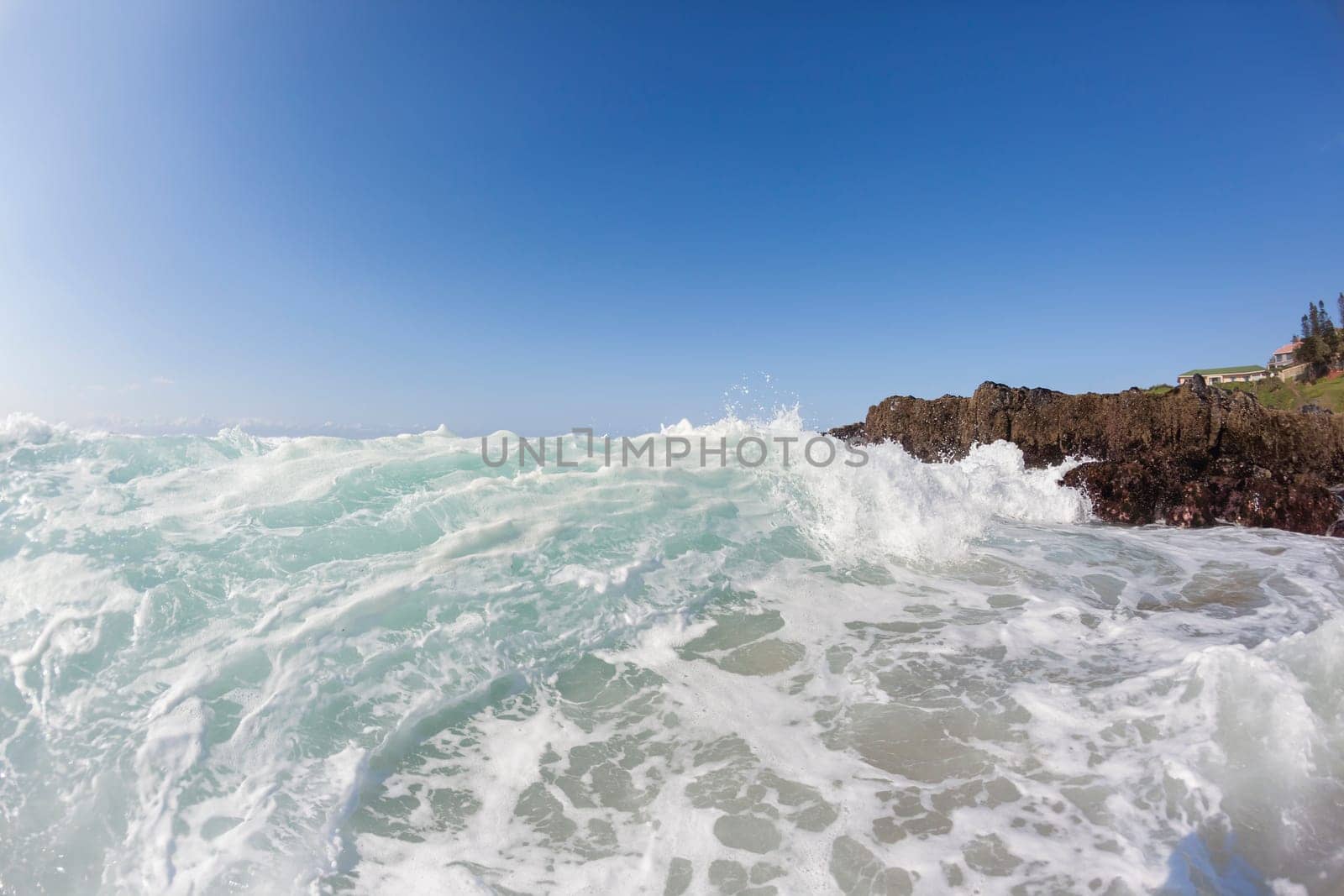 Ocean waves shore break crashing into rocks along beach coastline swimming closeup detail.