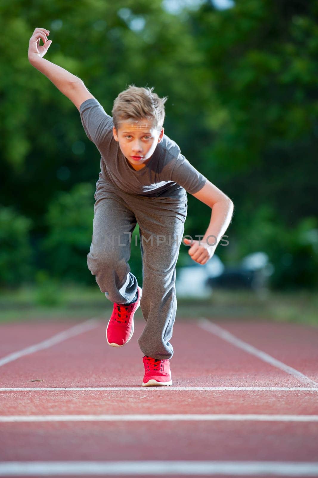 Frontal full-body view of a young male teenager on a tartan track towards the camera