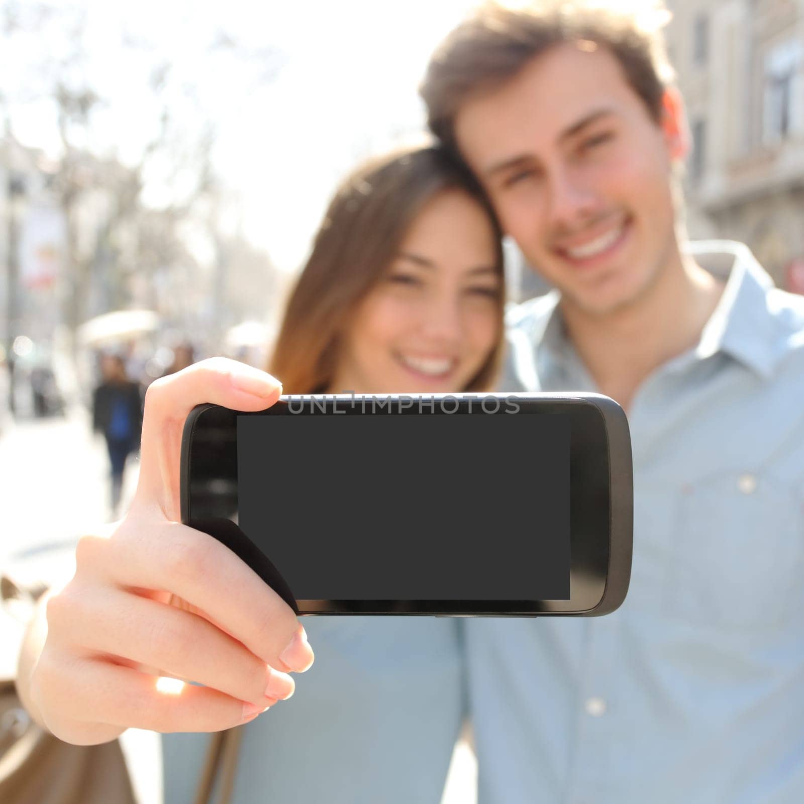 Happy couple or friends making a selfie photo with a smart phone and showing a blank screen to the camera