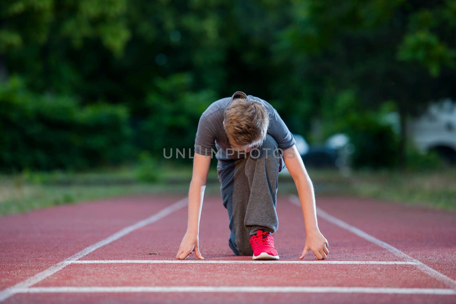Deep frontal full-body view of a young male teen in low-start position on a tartan track looking into the camera