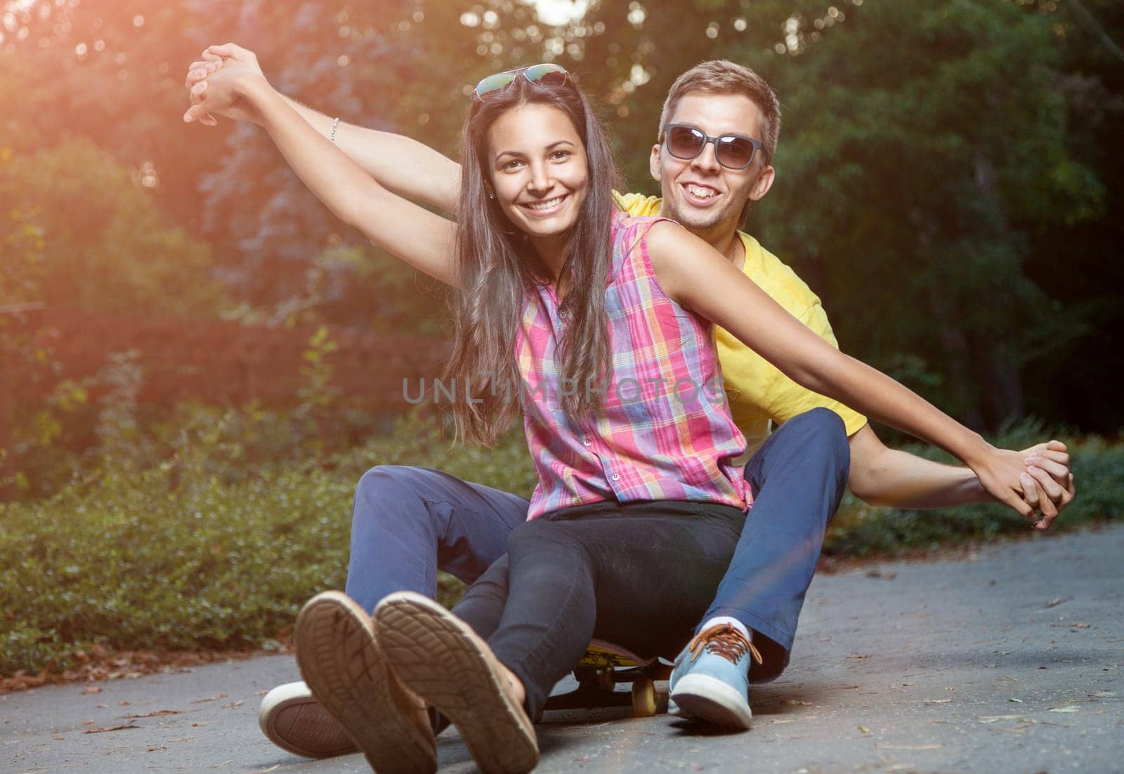 Young happy couple in love sitting on a skateboard outdoors