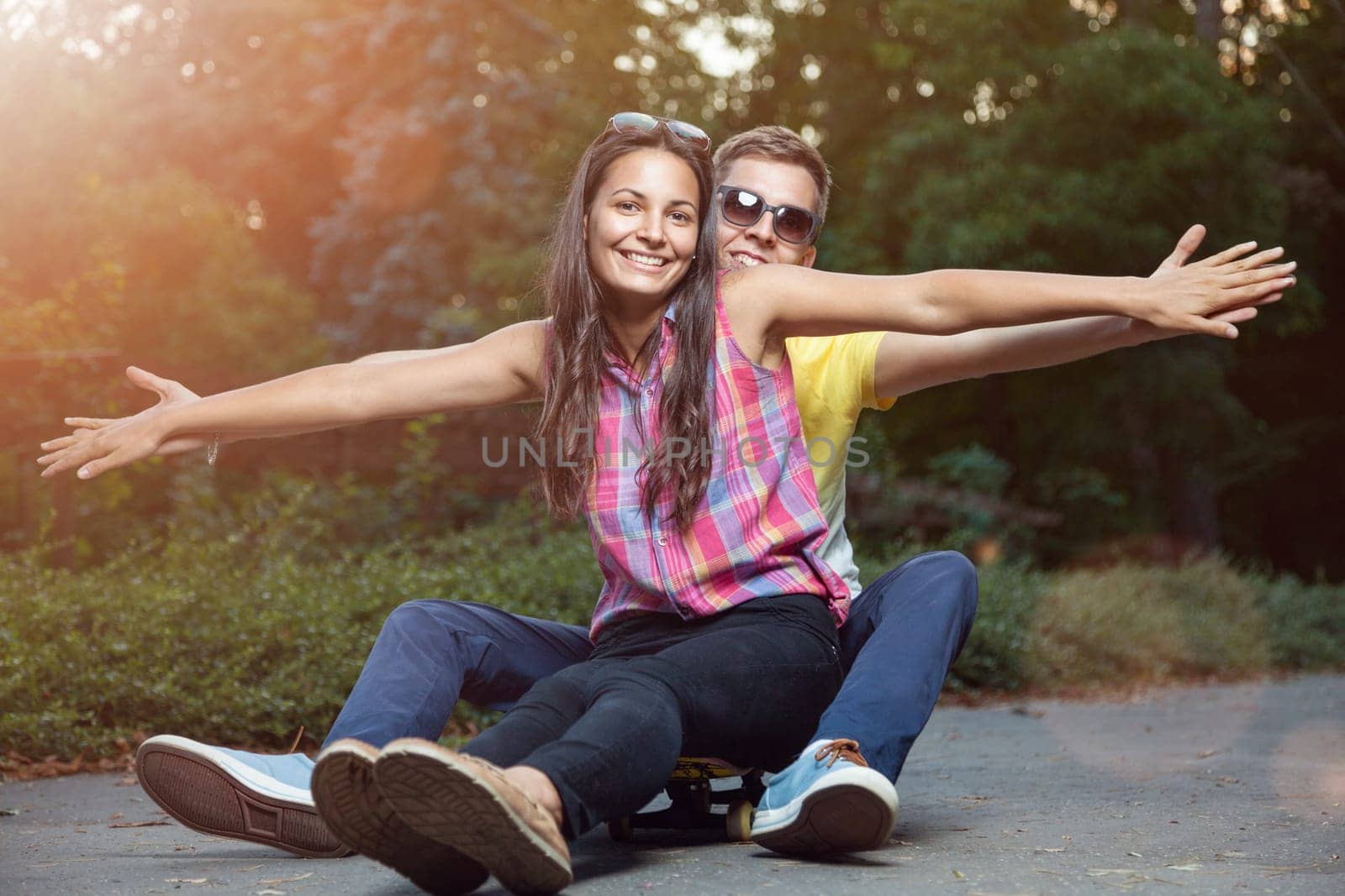 Young happy couple in love sitting on a skateboard outdoors