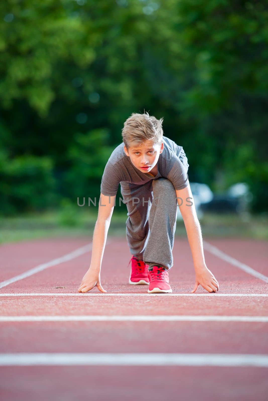 Deep frontal full-body view of a young male teen in low-start position on a tartan track looking into the camera