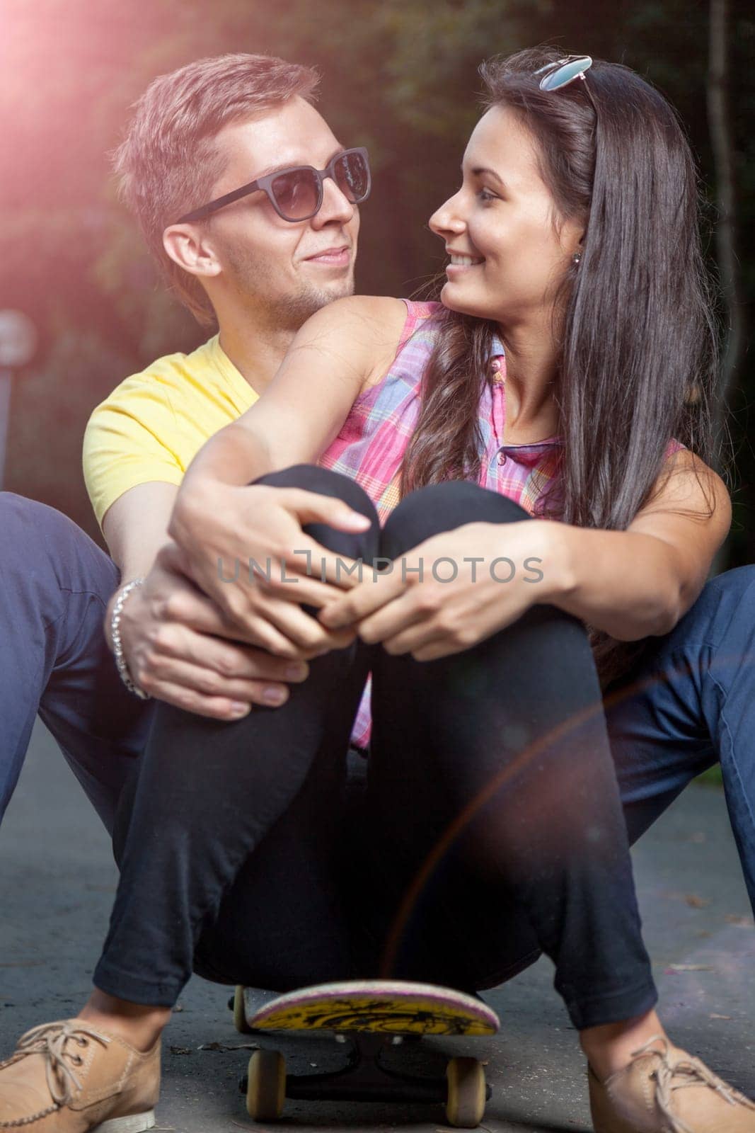 Young happy couple in love sitting on a skateboard outdoors