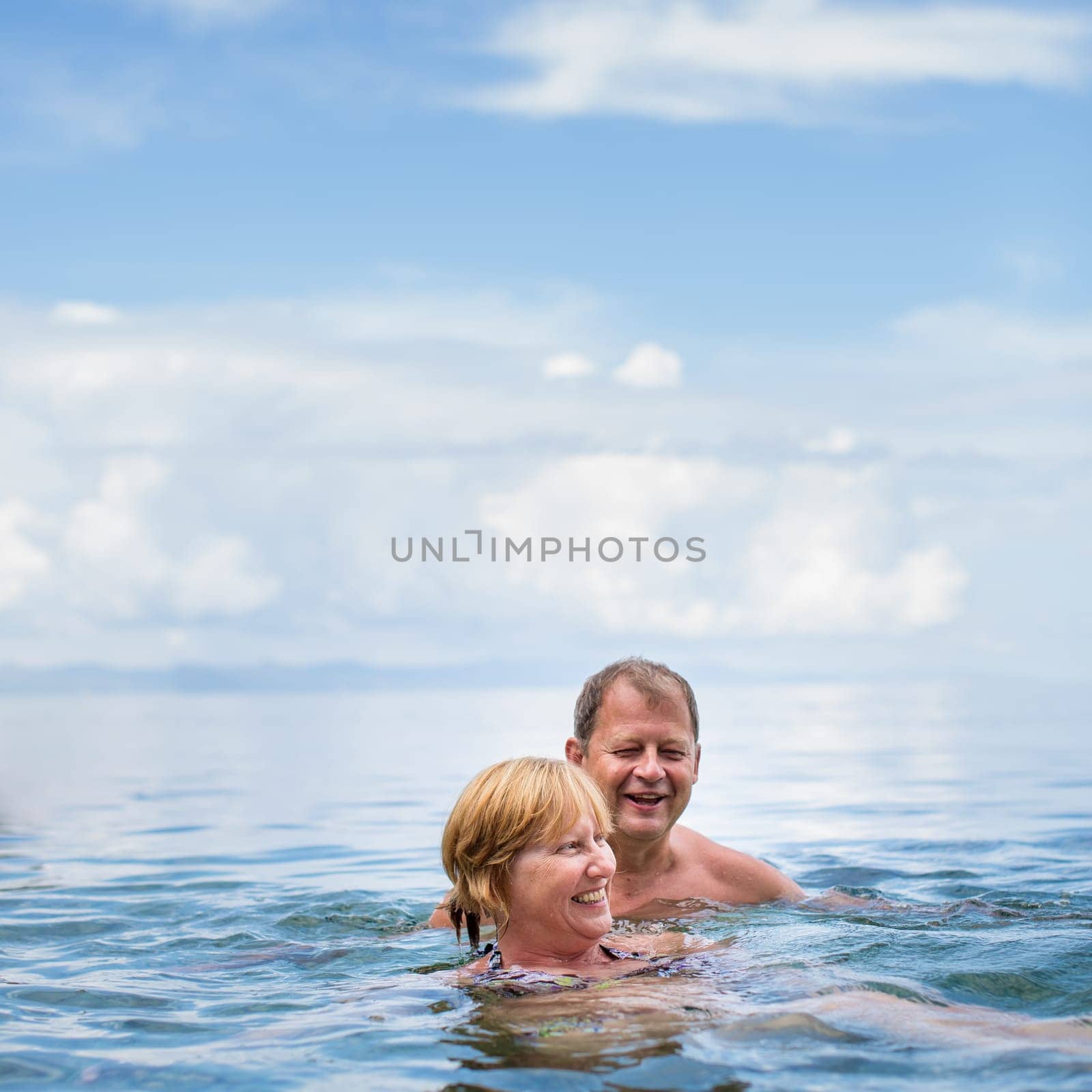 Senior couple enjoying the retirement on a seacost, having a swim in the sea, laughing togther, staying active and positive