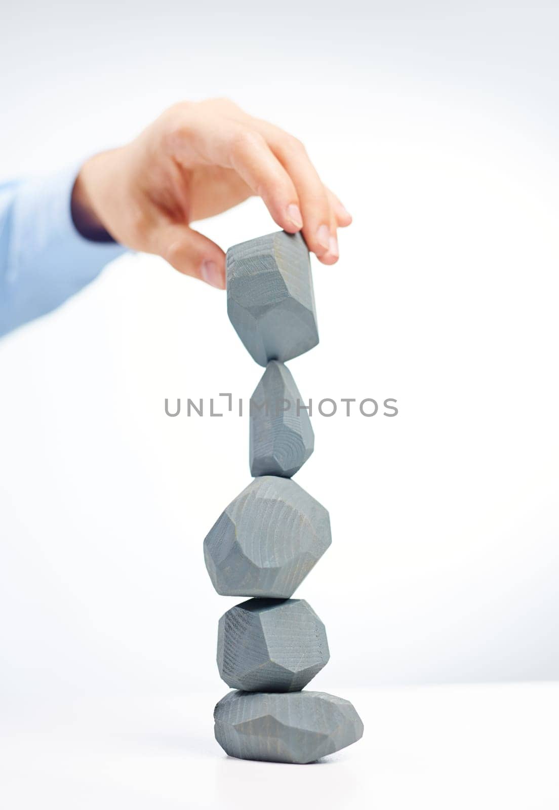 Human hand holding grey stone over stone tower