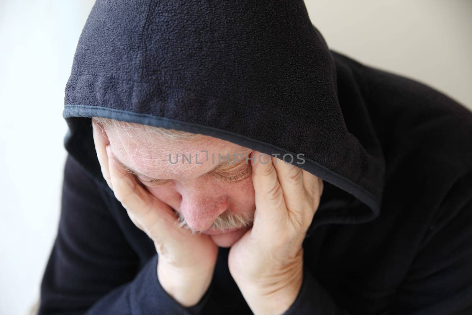 Senior man wearing a dark hoodie slumps in depression.
