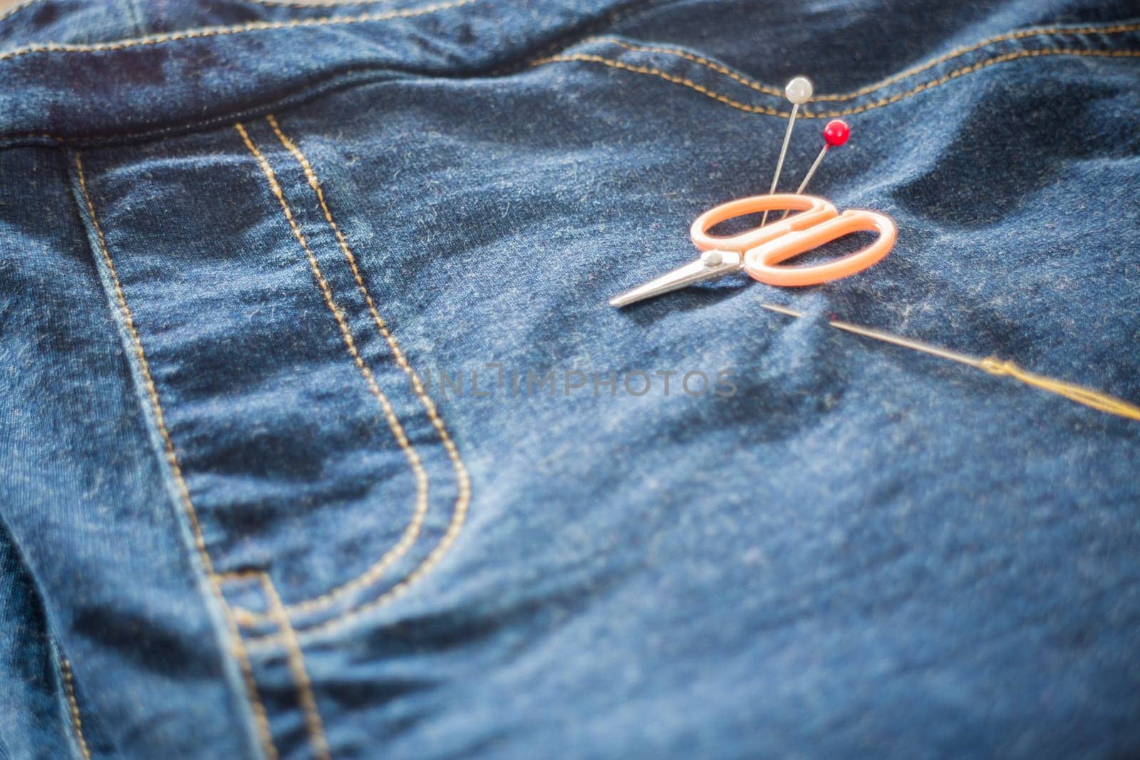 Needle with a thread through the jean, stock photo
