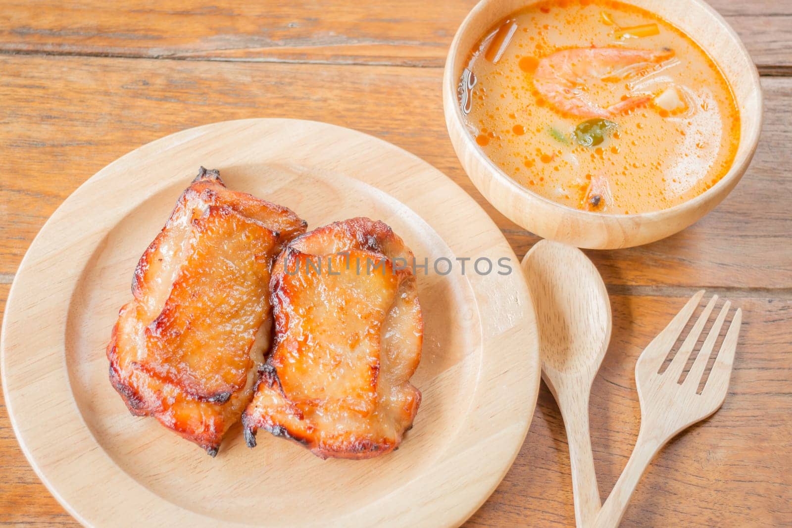 Chicken steak and spicy soup on wooden table, stock photo
