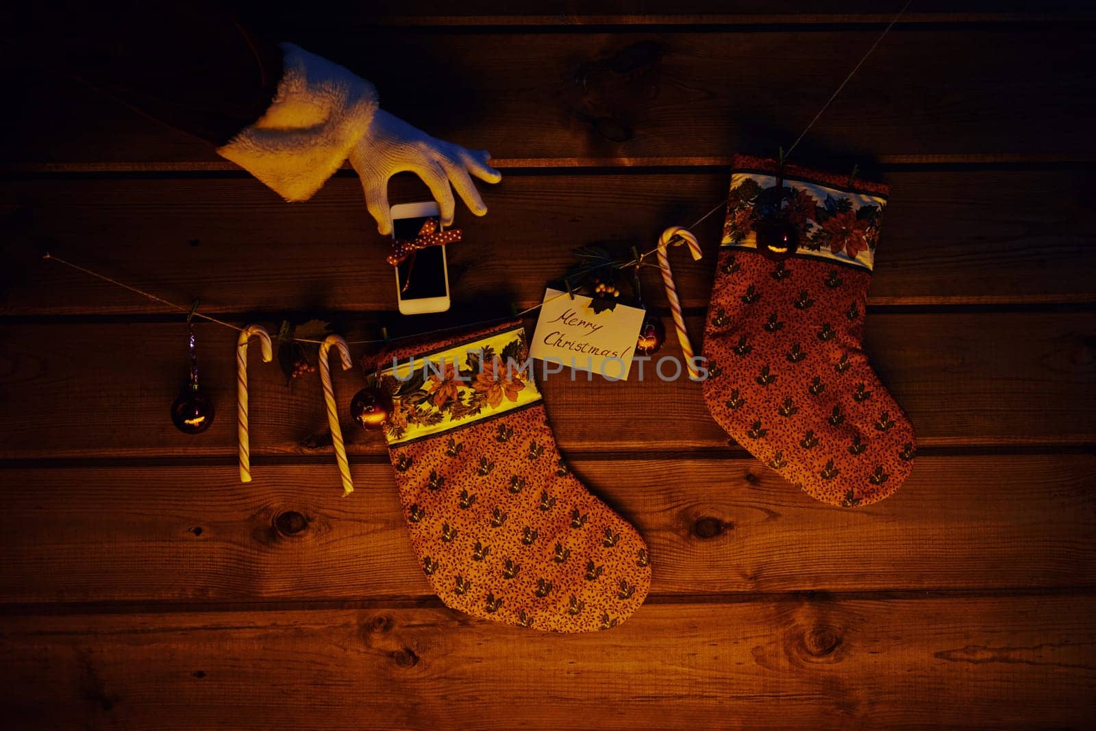Christmas socks, sugar canes, toy bubbles on wooden background and cellphone bound with ribbon in gloved Santa hand