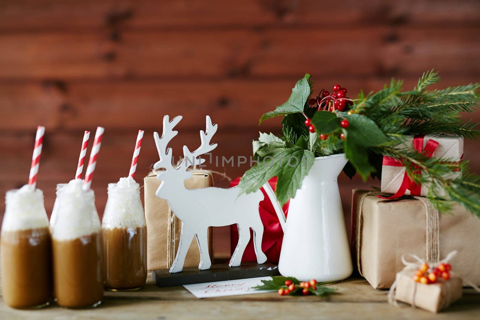 Toy deer, porcelain vase with guelder leaves and berries, bottles with hot chocolate topped with whipped cream and giftboxes on table in cafe