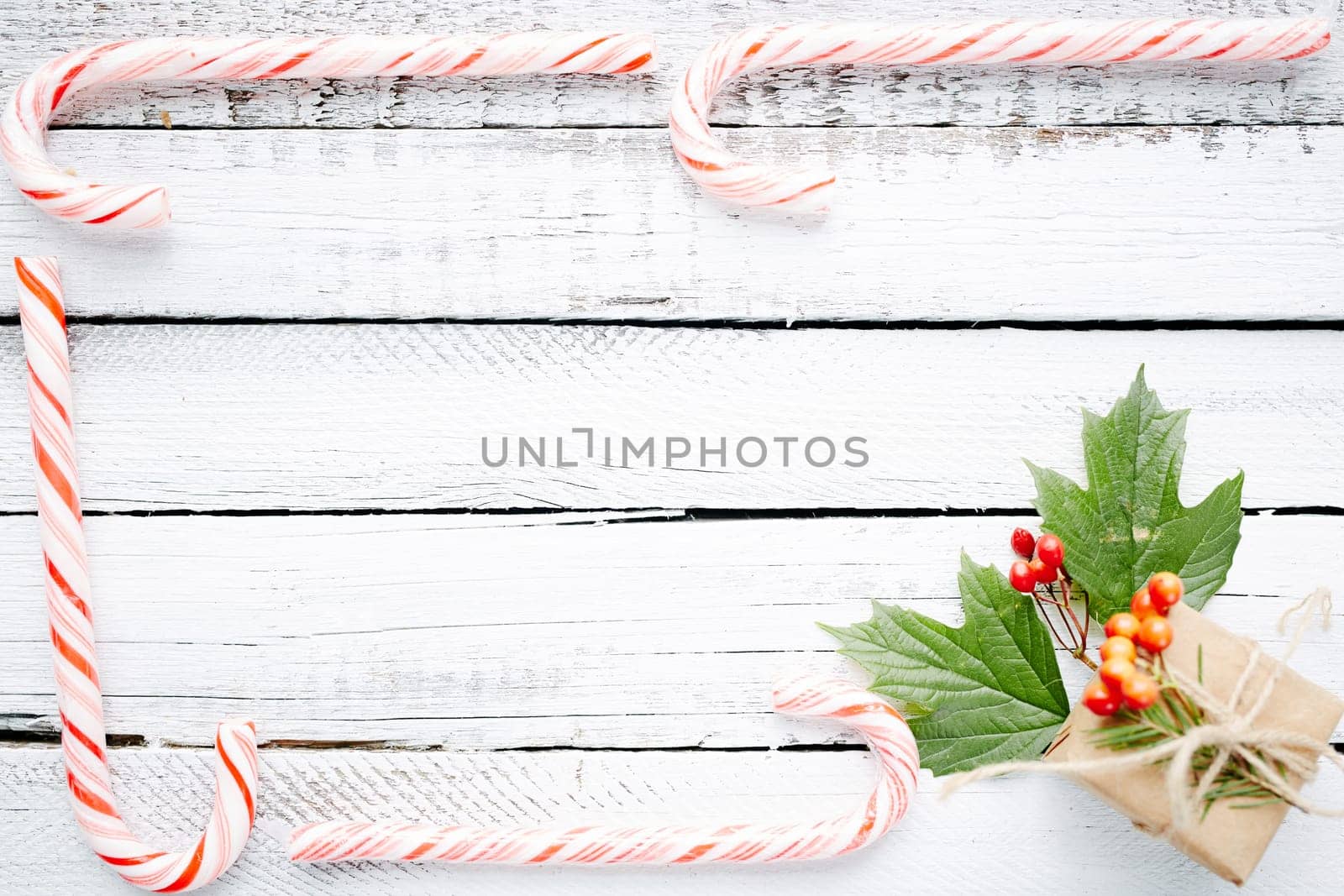 Christmas frame made up of candy canes and small package with guelder berries and leaves