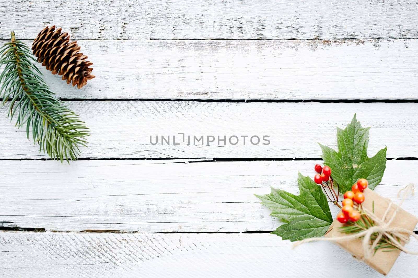 Gift in package, conifer branch, guilder leaves and berries over wooden background