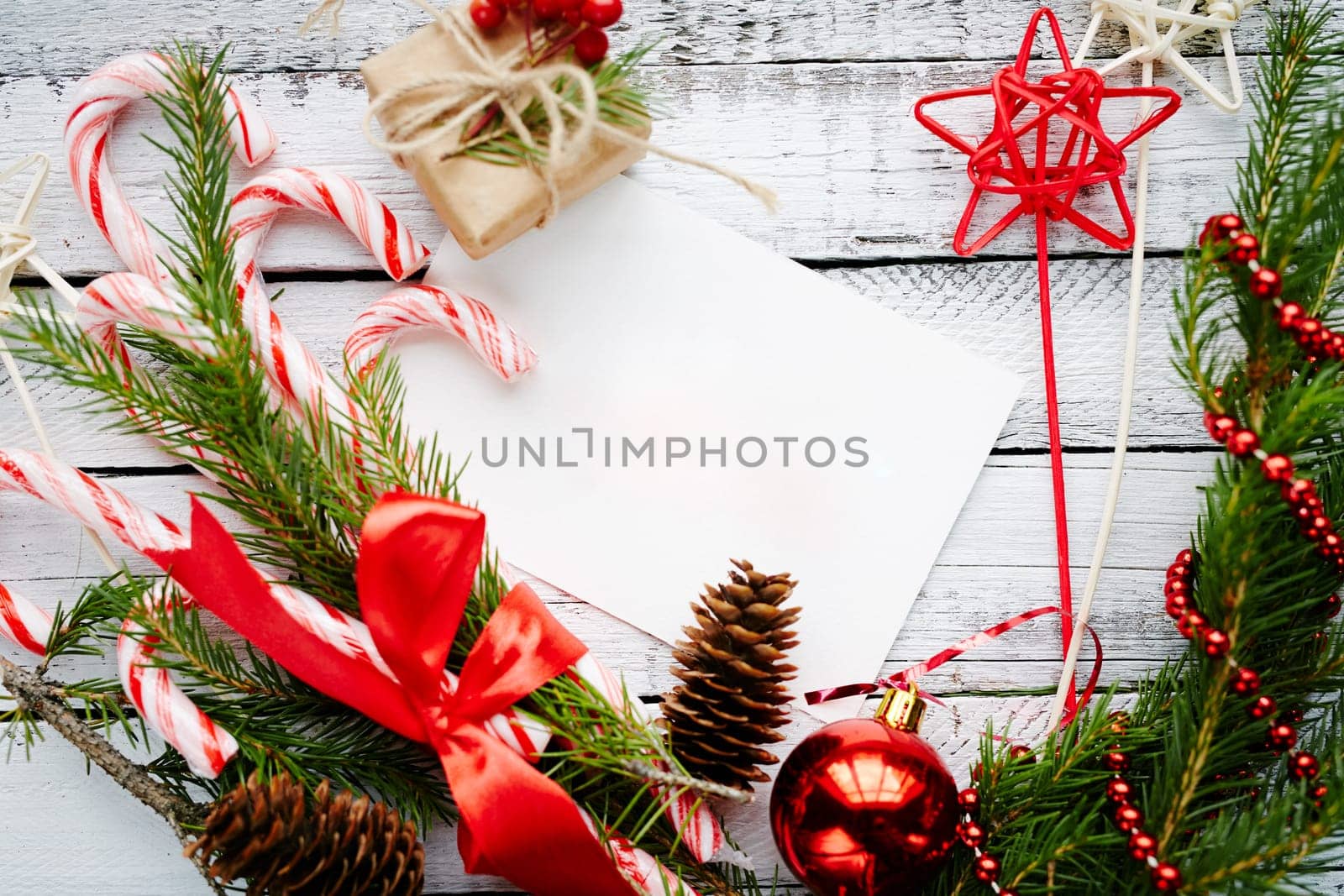 Christmas composition made up of conifer branches, cones, decorative bubble, stars, beads, candy canes and small giftbox on wooden background
