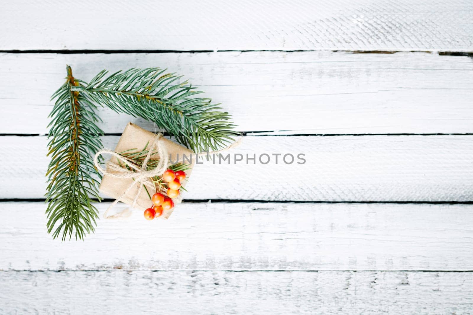 Gift in package and evergreen conifer branches over wooden background