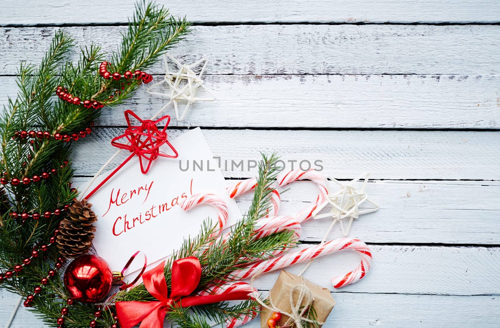 Christmas composition of conifer branches, cones, decorative bubble, stars, beads, candy canes, greeting card and small giftbox