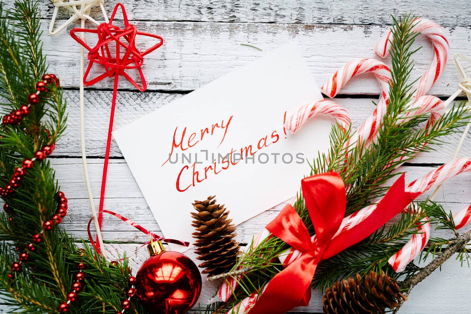 Christmas composition made up of conifer branches, cones, decorative bubble, stars, beads, candy canes and greeting card on wooden background