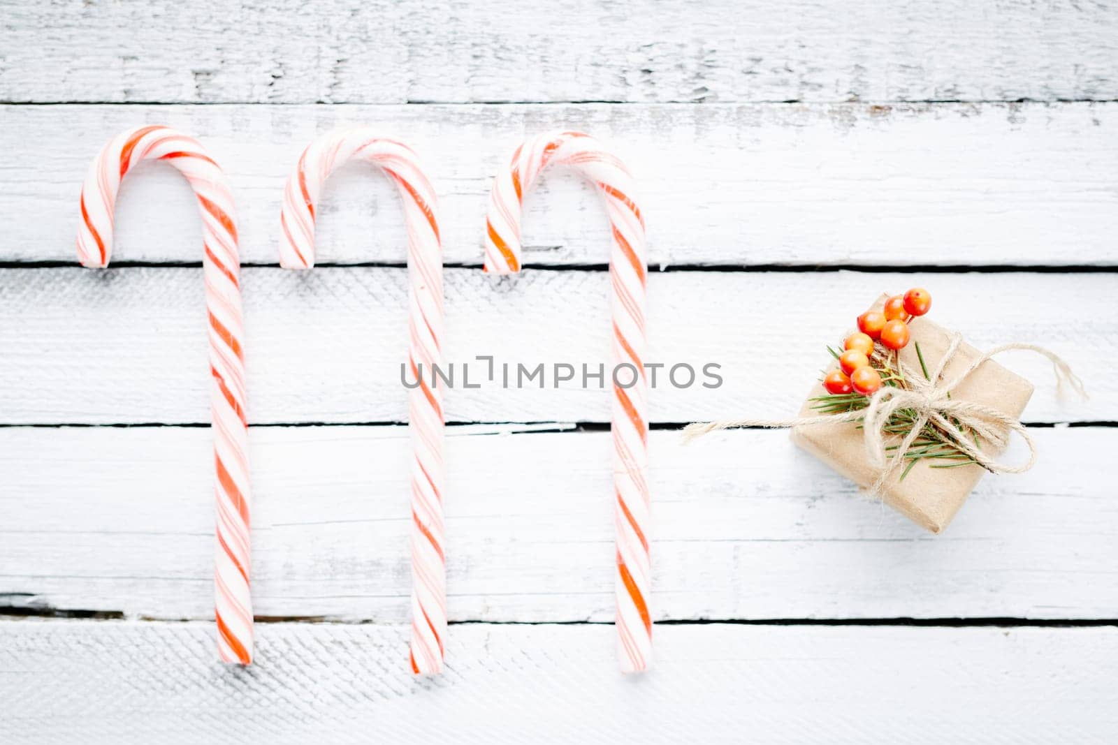 Candy canes and small package with gift over wooden background