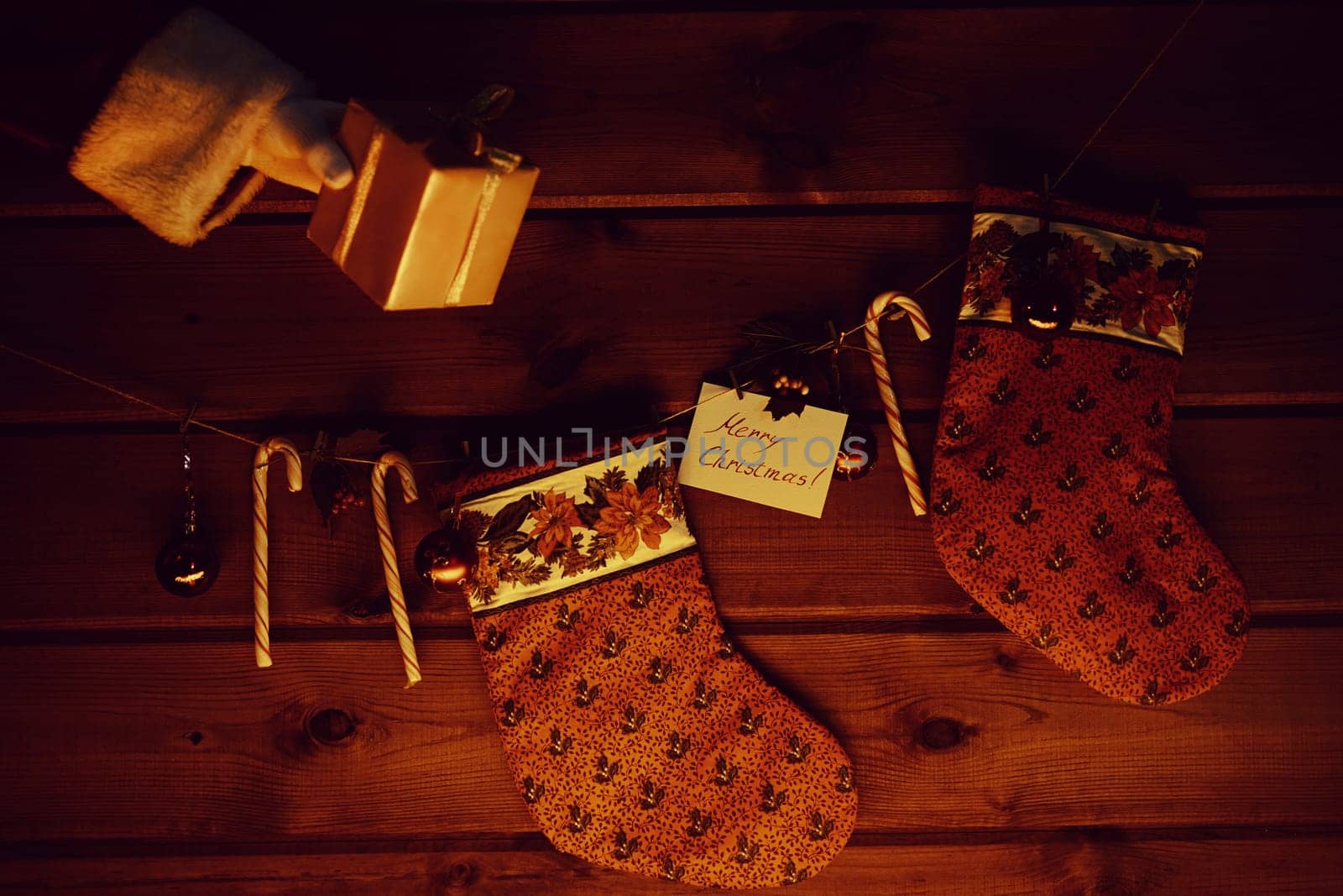Christmas socks, sugar canes, toy bubbles on wooden background and giftbox in gloved Santa hand