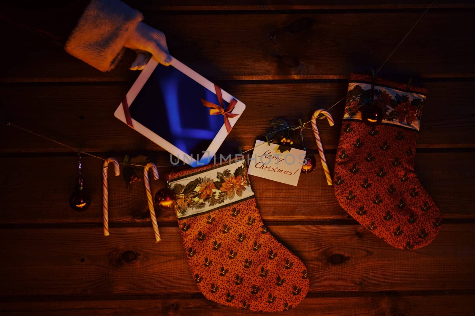 Christmas socks, sugar canes, toy bubbles on wooden background and touchpad bound with red ribbon held by Santa