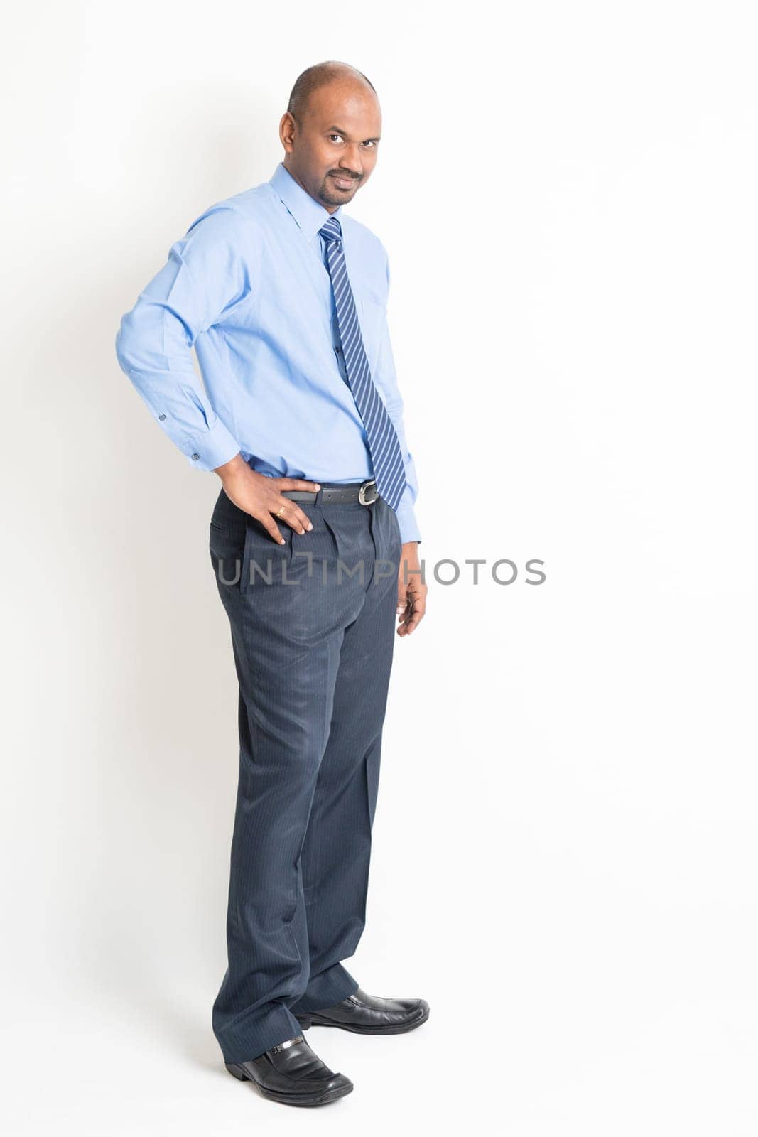 Portrait of full body mature Indian business man with blue shirt standing on plain background.