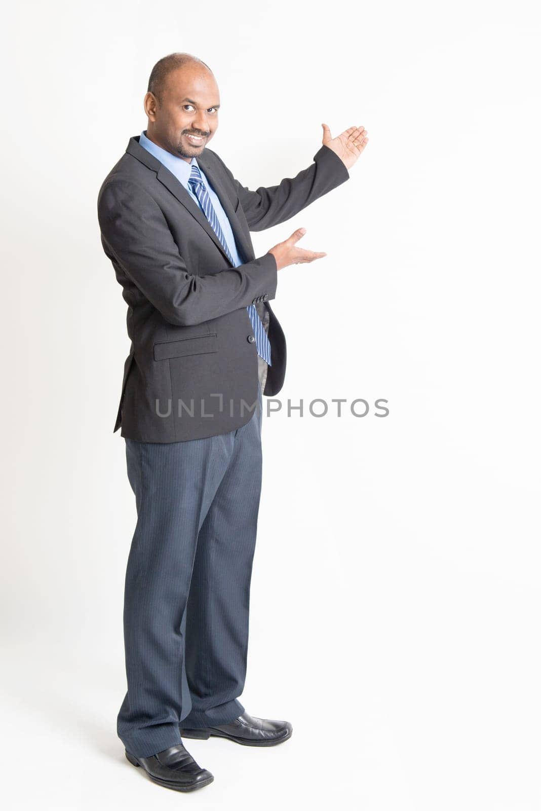 Full body mature Indian business man showing something at blank space, standing on plain background.