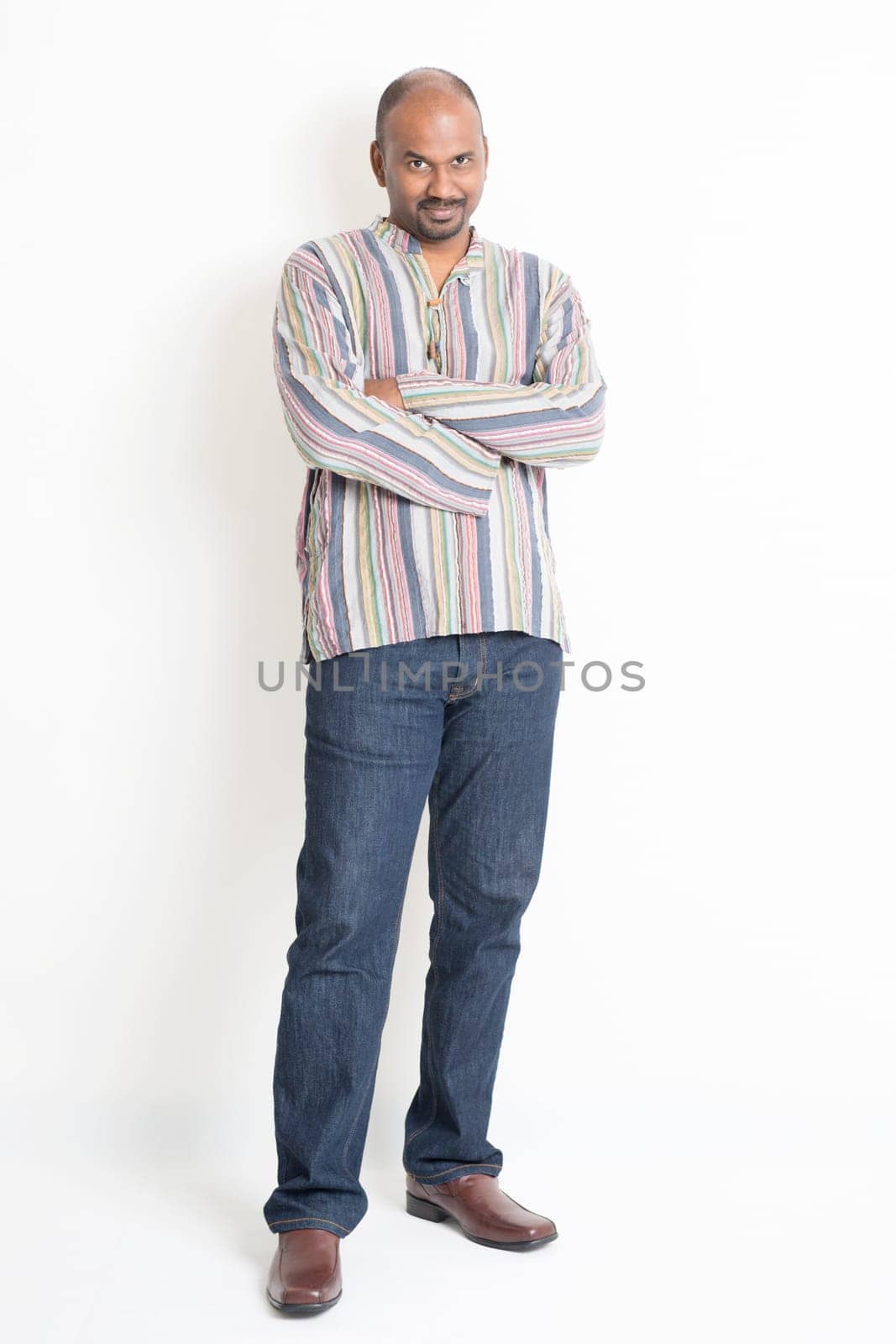 Full body confident mature Indian man in casual wear standing on plain background with shadow.