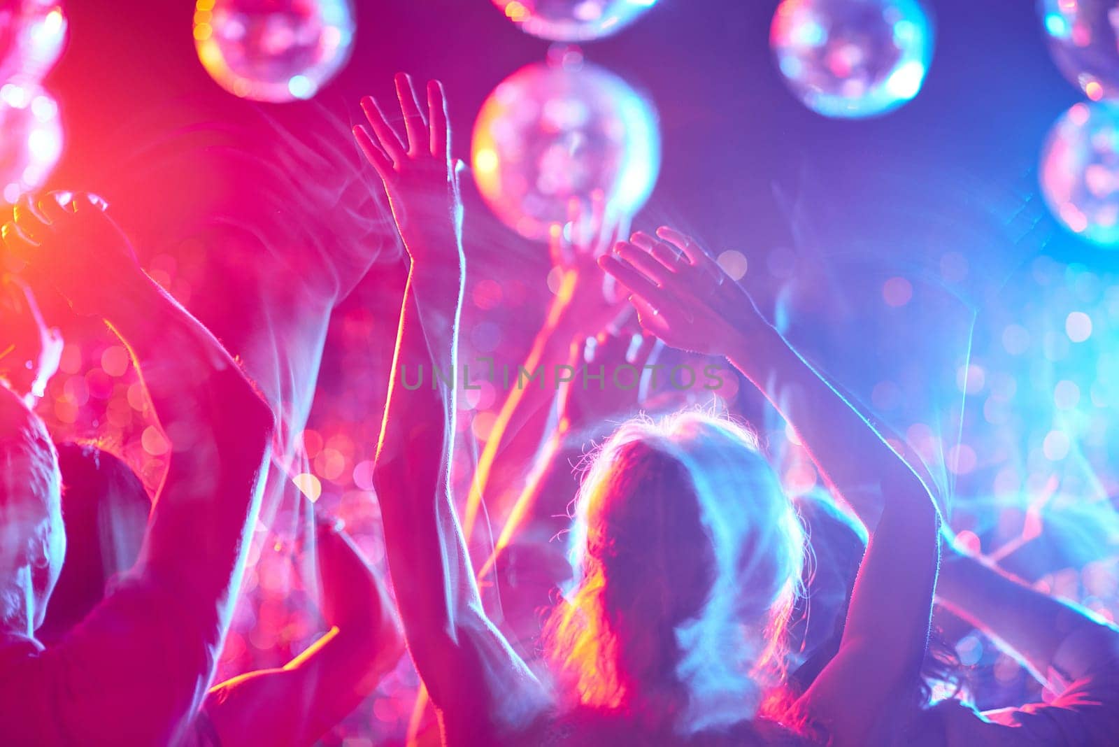 Crowd of people with raised arms dancing in night club