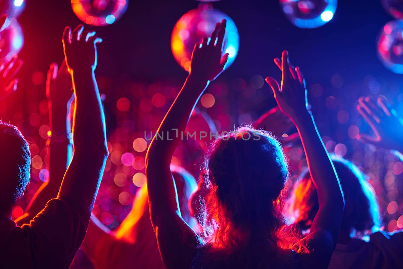 Group of young people with raised arms dancing in night club