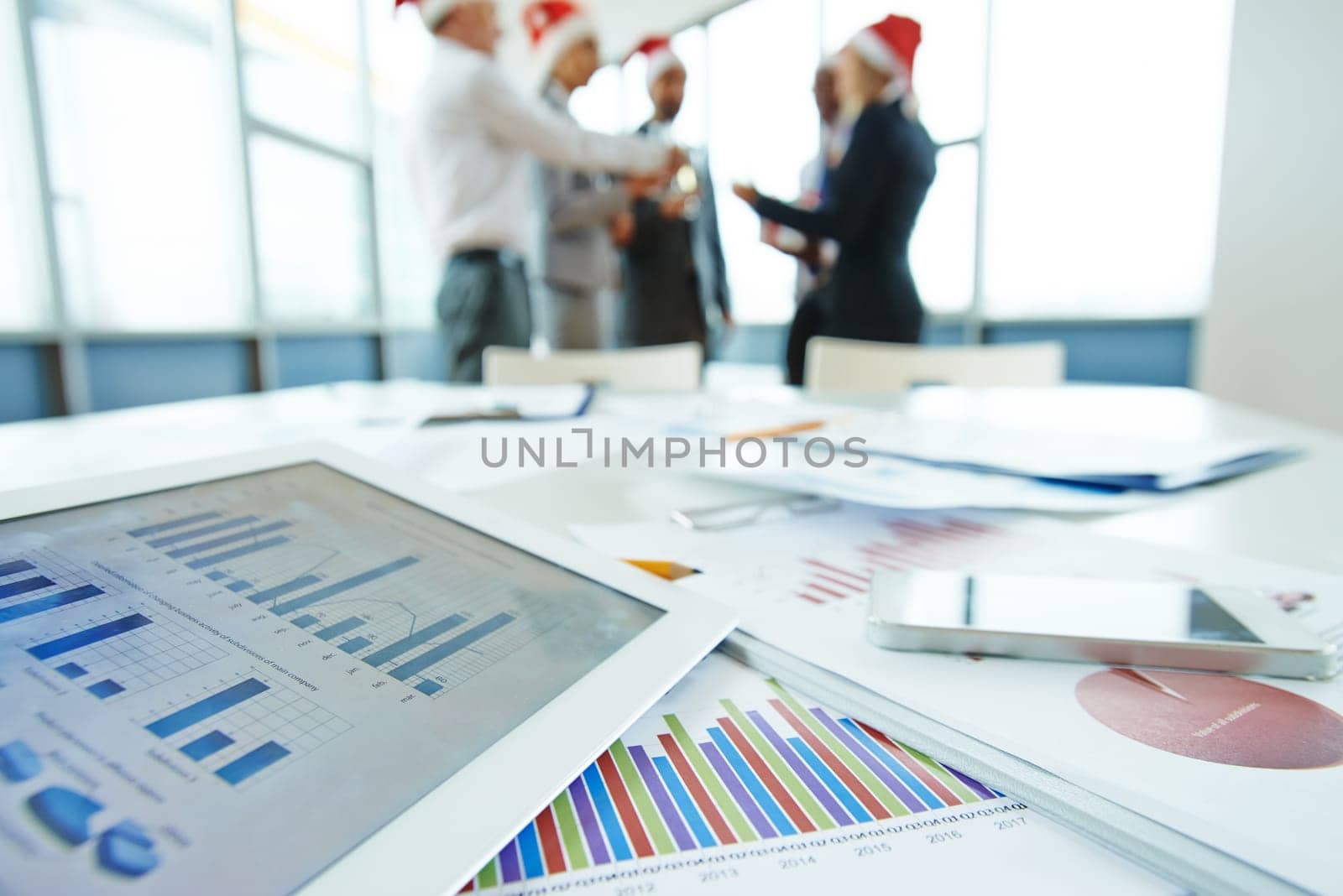 Documents and touchpad with data at workplace on background of toasting colleagues