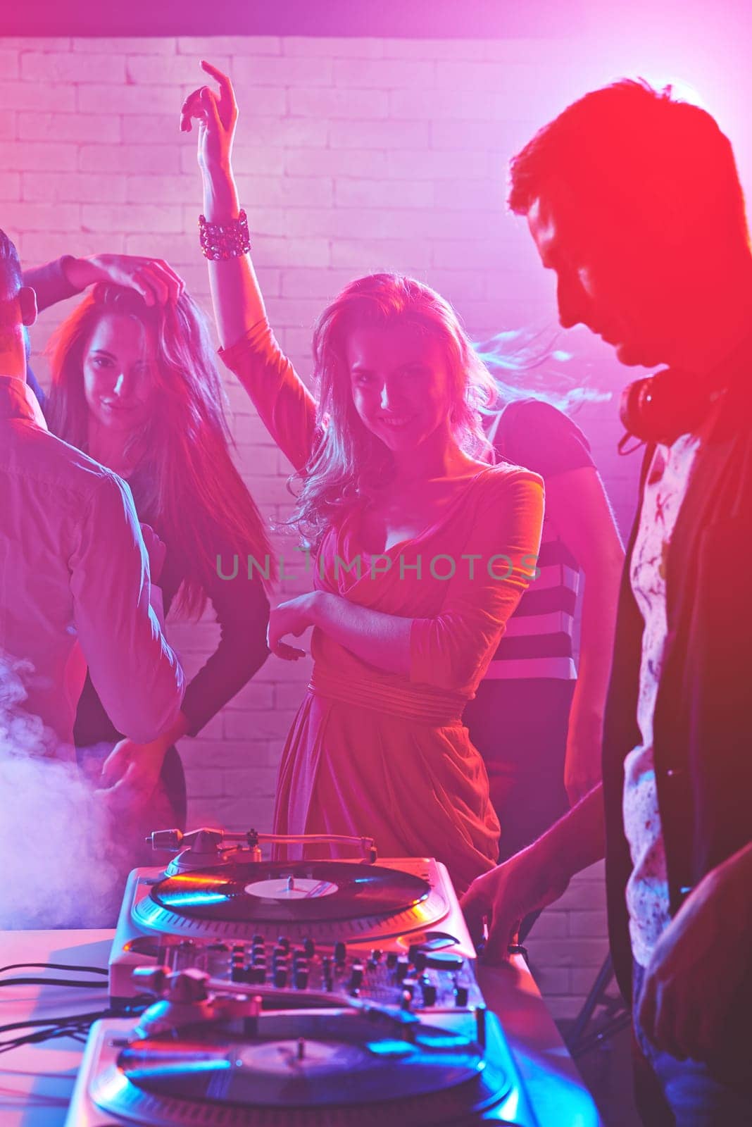 Dancing girls enjoying party by turntables of deejay adjusting sound