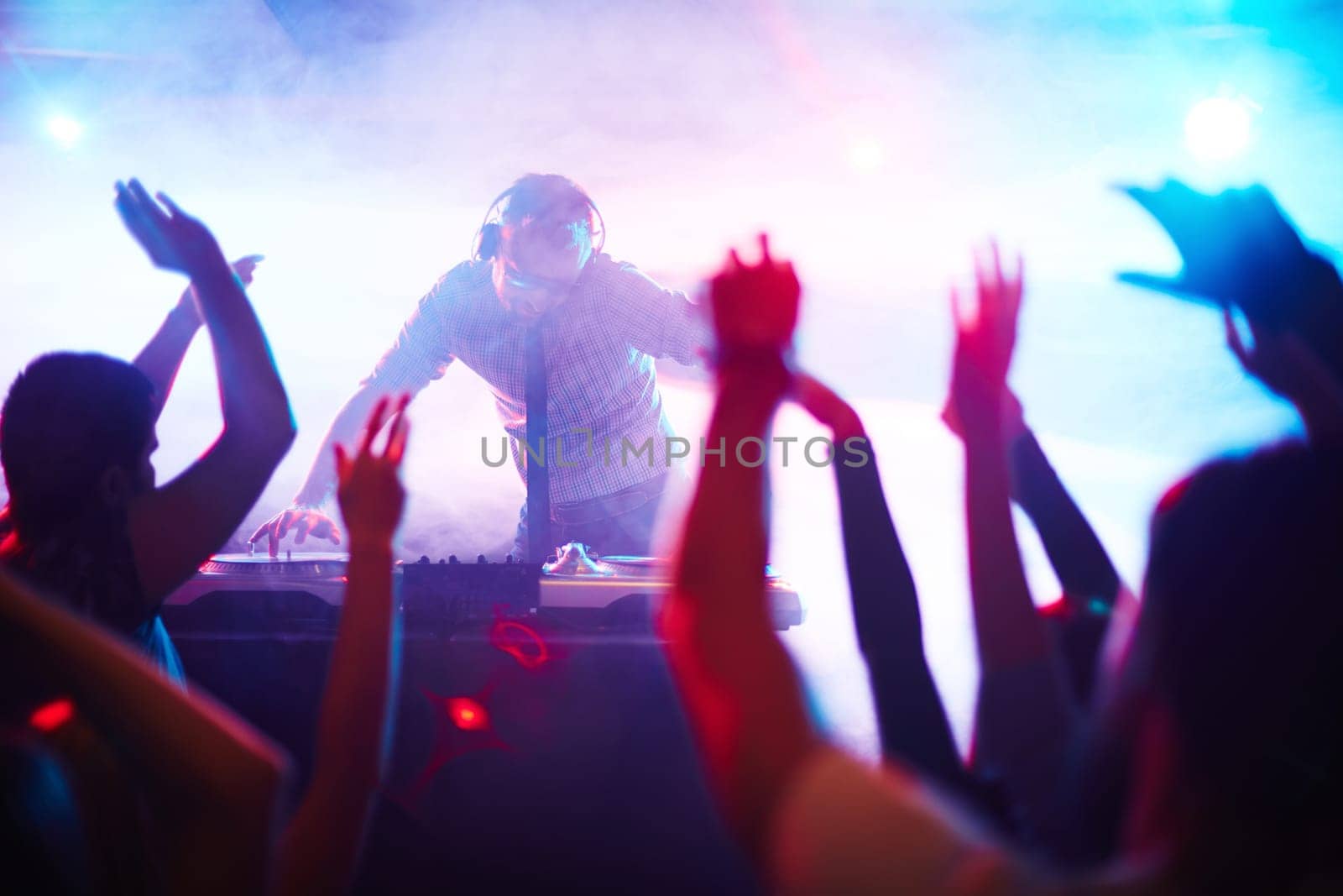 Energetic deejay standing by turntables in front of dancing crowd