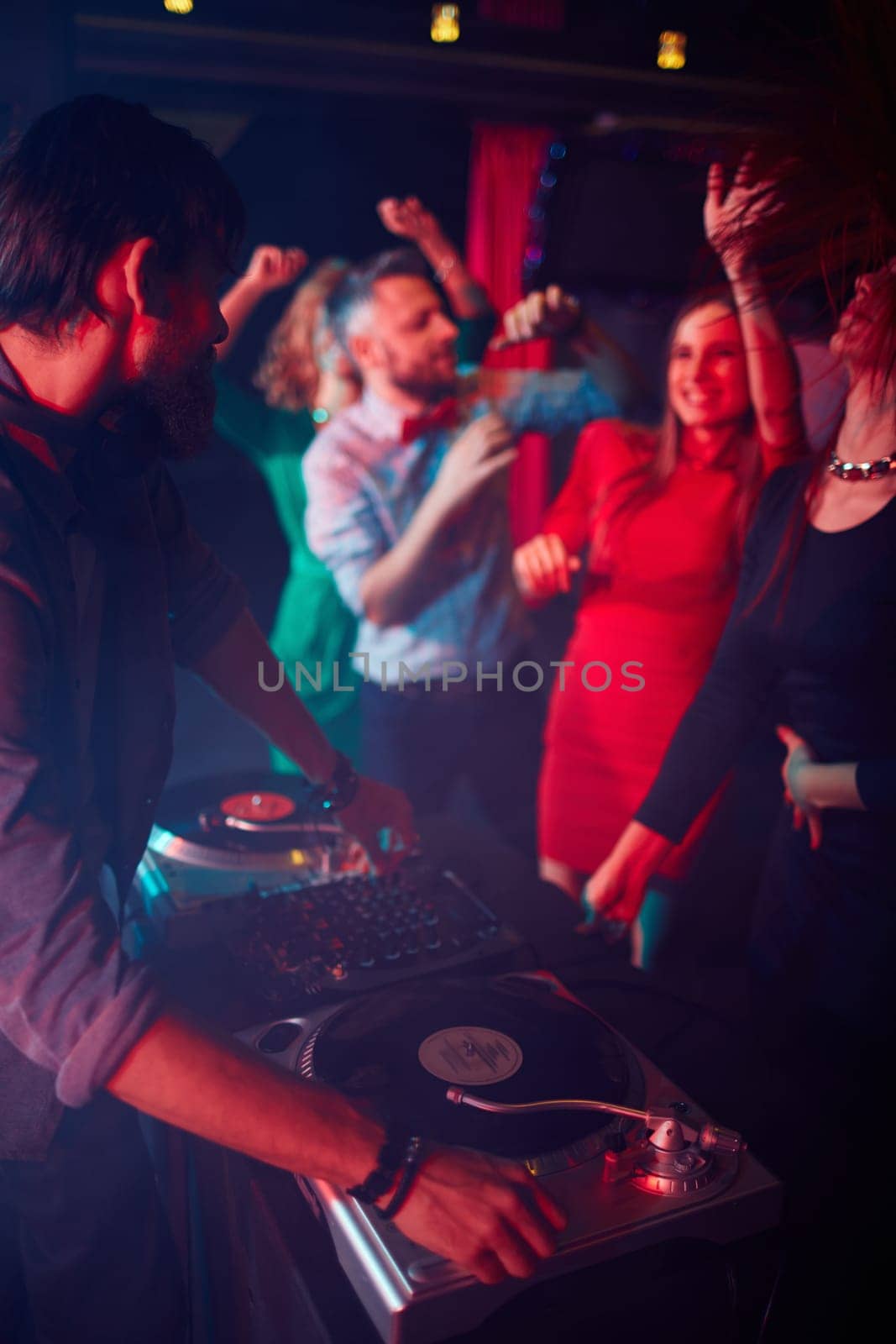 Modern deejay adjusting sound on turntables with group of dancing girls near by
