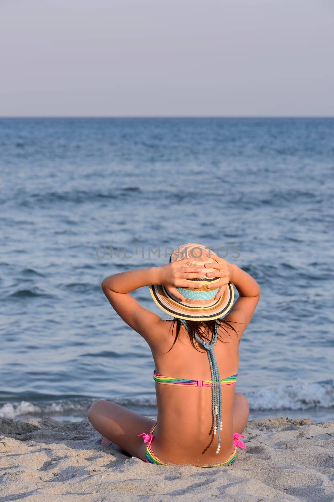 Little girl on the beach at sunset, portrait smiling with a large hat.
