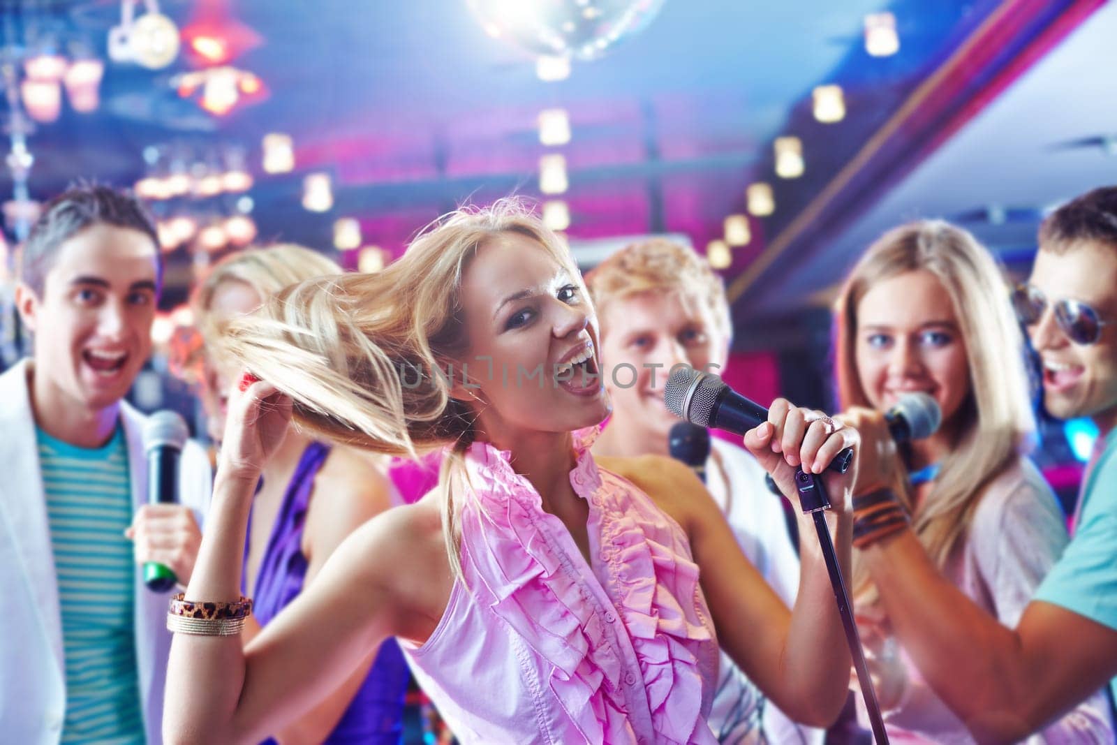 Pretty girl singing at party on background of happy friends