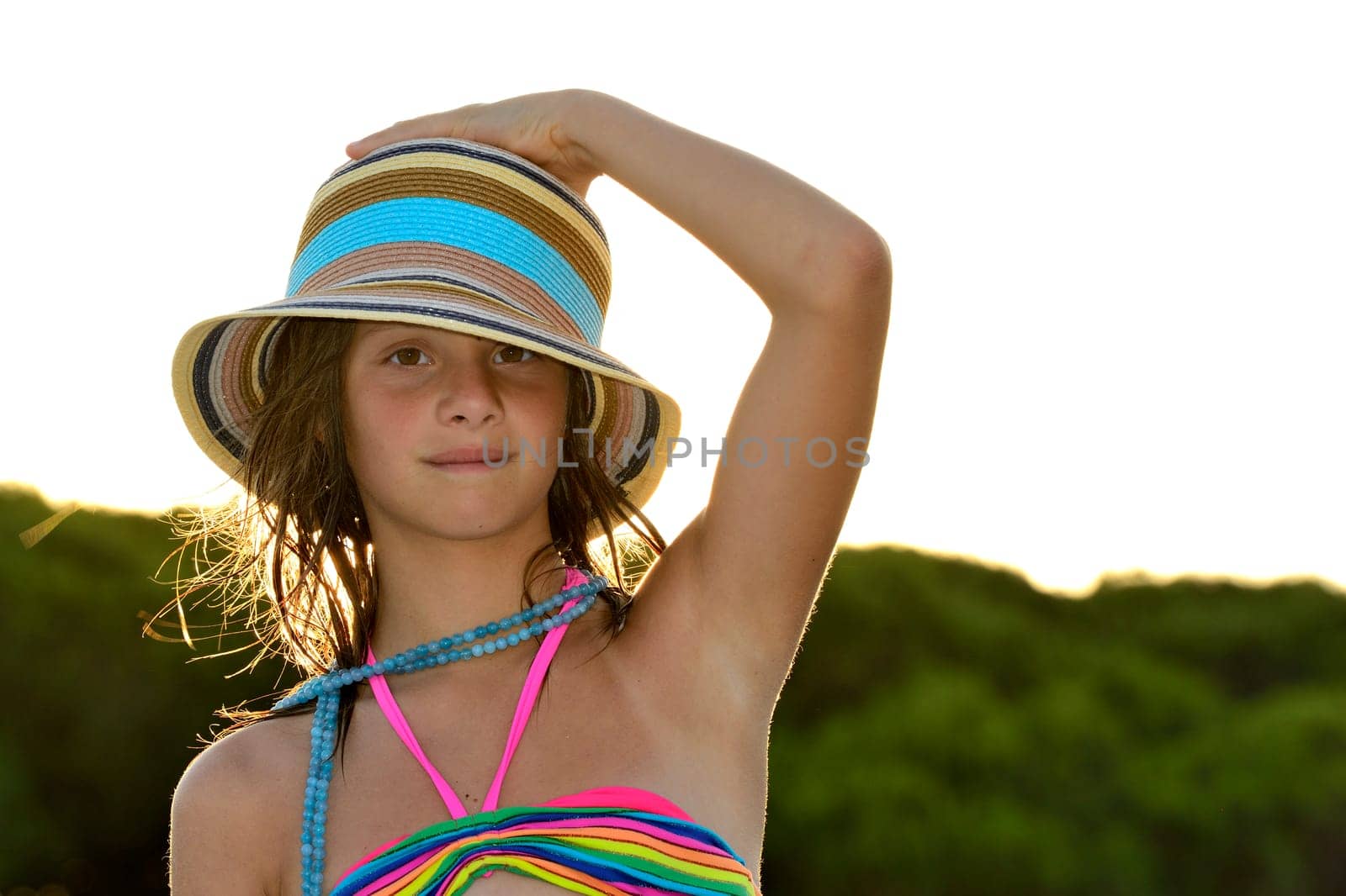 Little girl on the beach at sunset, portrait smiling with a large hat.