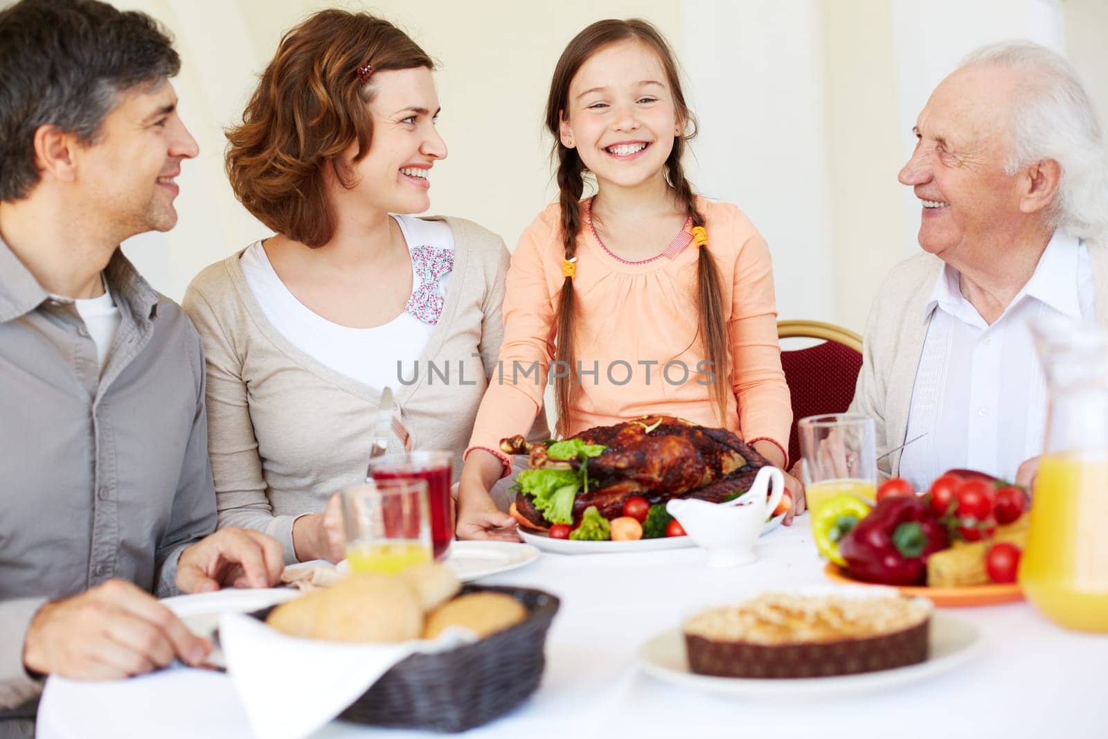 Happy family sitting at Thanksgiving table and looking at cute girl with roasted turkey