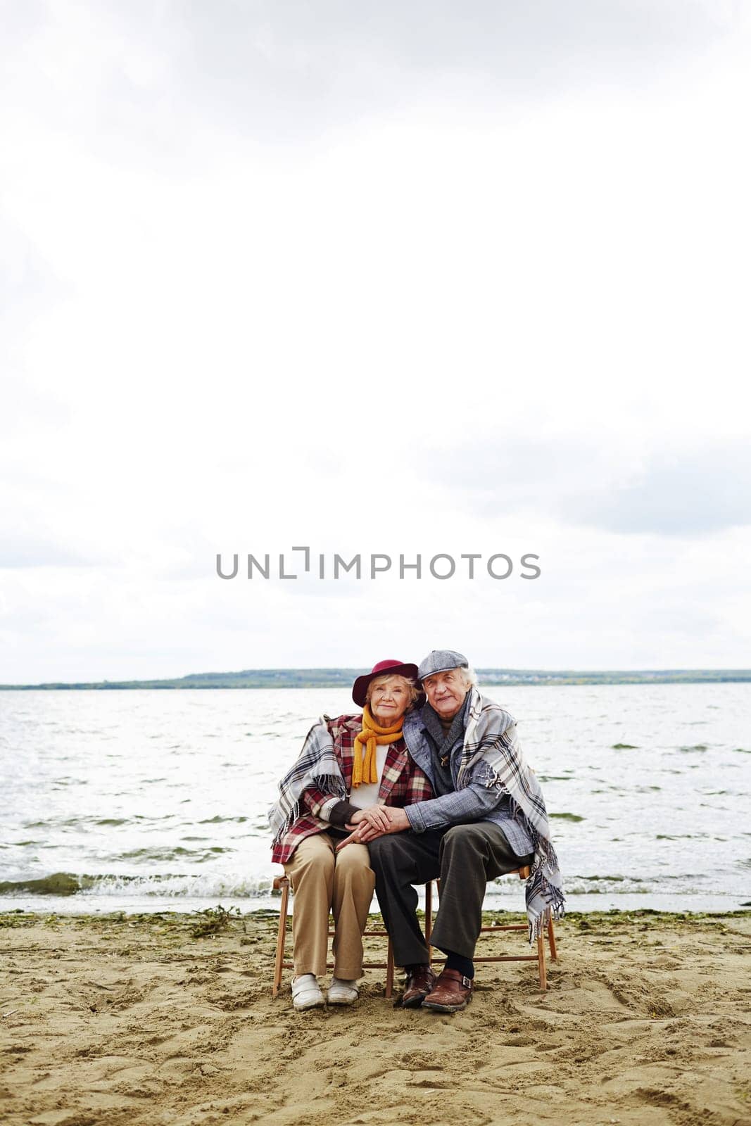 Retired seniors sitting by seaside and looking at camera