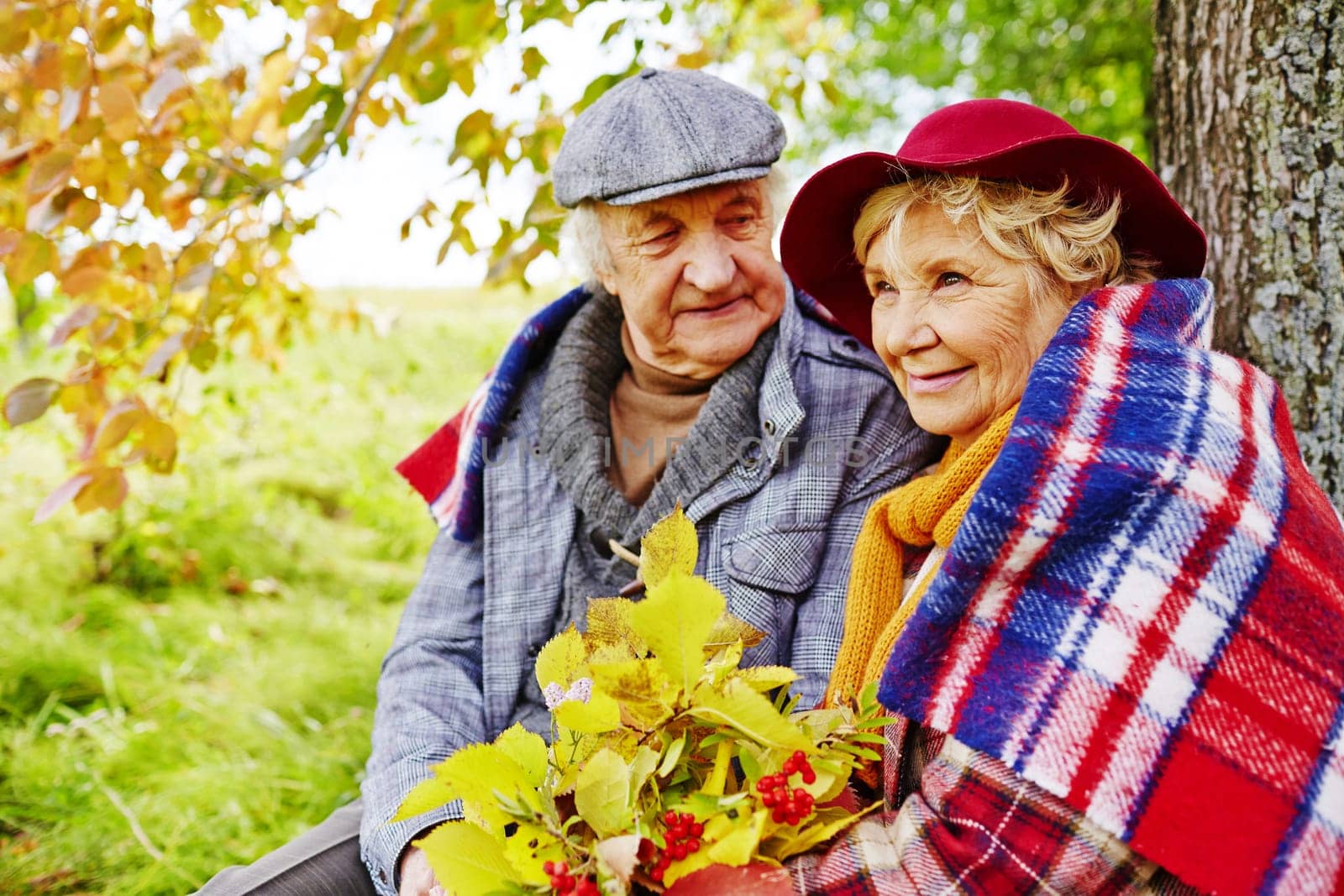 Affectionate senior couple having rest under tree on autumn day